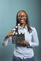 Portrait of african american female movie director happily holding clapperboard, ready for shooting. Smiling female filmmaker poses with film slate in hand, looking at camera with enthusiasm. photo