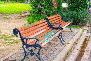 Old wooden benches sit on a stone path amidst the lush greenery and flowering plants of a park photo