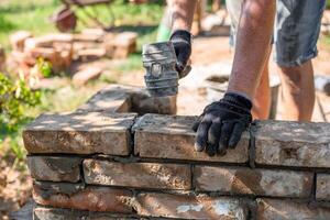 worker wearing a glove and using a rubber mallet places a brick in place in a newly erected brick wall of a barbecue photo