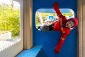 Child with red raincoat of firefighter clings to a rope in a playground during rain. photo