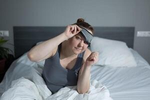 A woman is lying in bed, gracefully removing her sleep mask as another day begins photo