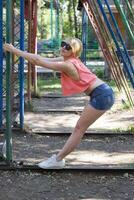 Girl Smiling Joyfully While Stretching Between Playground Swings at a Sunny Park photo