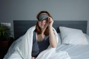 A Young Woman Waking Up in a Cozy Bedroom Surrounded by Soft Blankets and a Sleep Mask photo