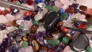 A collection of vibrant chakra stones is carefully sorted using tweezers, highlighting their diverse colors and textures video