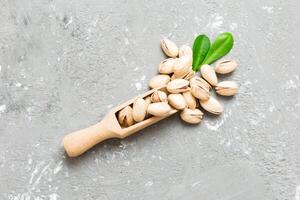 Close-up of tasty pistachio nuts in spoon with leaves on table background photo