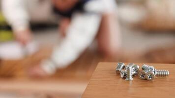 Close-up of metal screws on a table with blurred background of furniture assembly in progress video