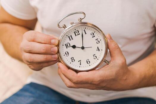 a man sets an alarm clock while sitting on the couch, close-up without a face, the concept of deadline and time control photo
