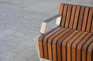 a wooden bench with metal arms sitting on a concrete sidewalk photo