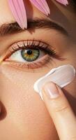 Closeup of womans face with green eye pink flower petals and cream application. photo
