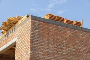 Workers are busy constructing a brick building, stacking wooden materials on the roof against a clear blue sky backdrop photo