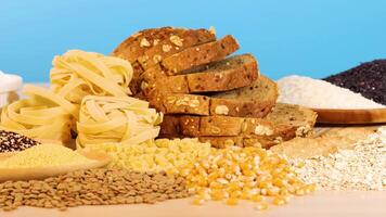 A variety of grains, pasta, and bread displayed on a wooden surface with a bright blue backdrop video
