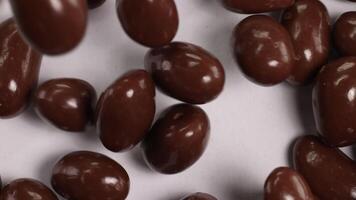 Chocolate-covered peanuts cascade onto a white surface, creating a dynamic and appetizing visual with smooth, glossy textures video