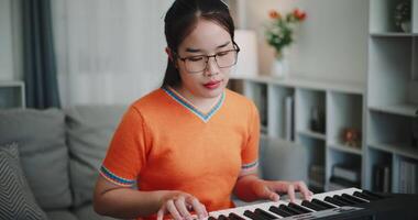 Handheld shot, Young Asian woman is relaxing and enjoying playing music on an electronic keyboard in a quiet house. Leisure activities at home video