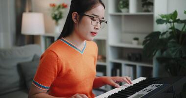 Handheld shot, Young Asian woman is relaxing and enjoy playing music on an electronic keyboard in a quiet house. Leisure activities at home video