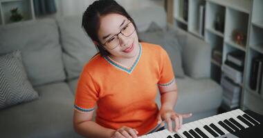 Handheld high angle view shot, Beautiful Asian woman playing the keyboard with happy smile in cozy living room. Enjoy a relaxing weekend activity video