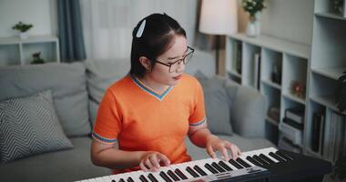 Handheld high angle view shot, Young Asian woman is relaxing and enjoying playing music on an electronic keyboard in a quiet house. Leisure activities at home video