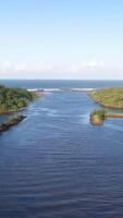 A serene aerial view of a river flowing towards the ocean, surrounded by lush greenery under clear blue skies video