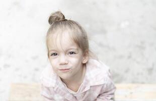 Close-up portrait of a young girl on a light background, gazing directly into the camera. Her innocent expression and soft natural light create a gentle and heartfelt moment. photo