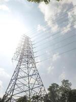 Low-angle shot of an Ultra High Voltage Power Line tower. An electrical distribution tower with bright sunlight, few clouds, and a clear sky in the background. Electrical technology industry. photo