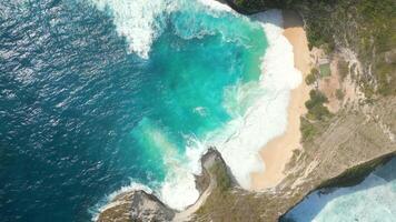 Aerial top-down view of turquoise ocean waves crashing on white sand at Kelingking Beach, Nusa Penida Island, Bali, Indonesia. Perfect for travel, nature, summer, and tropical paradise themes. video