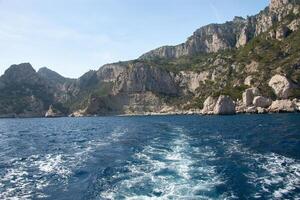 Boat tour along the coast of the Calanques in Marseille with crystal-clear waters and rocky mountains under a blue Mediterranean sky photo