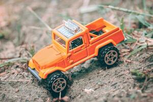 Horizontal photo of miniature 4x4 pickup truck stuck off-road in forest diorama, trying to climb back up. Concept of travel, adventure and overcoming obstacles.