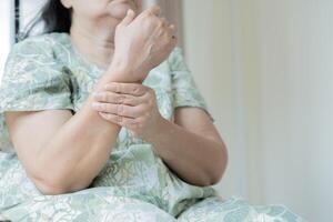Mature Asian woman suffering from pain in hand at home, space for text. Rheumatism symptom. photo