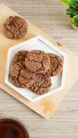 Top view of chocolate cookies treats on a white plate with a cup tea isolated on wooden textured background photo
