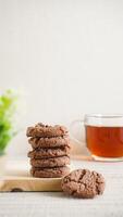 Stack of sweet chocolate cookies on a white plate with a cup of tea isolated on light background photo
