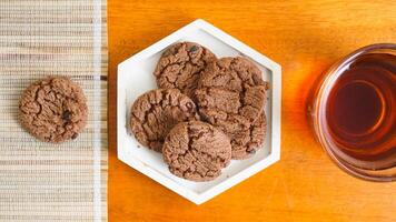 Top view of chocolate delicious chips cookies on a white plate with a cup of tea isolated on wooden textured background photo