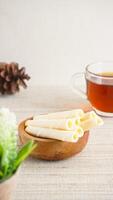 Crispy rolled wafer snack on serving plate with a cup of tea isolated on wooden textured background photo