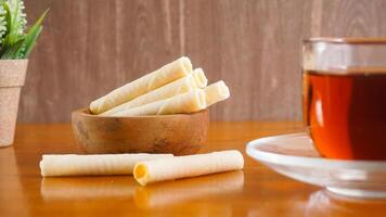Wafer rolls snack with sweet cheese cream filling serving on plate with a cup of tea for enjoyment isolated on wooden background photo
