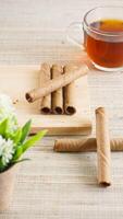 Crispy chocolate wafer roll on a wooden board with a cup of tea for enjoyment isolated on wooden textured background photo