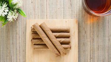Top view of delicious chocolate wafer roll on a wooden board with a cup of tea isolated on wooden textured background photo