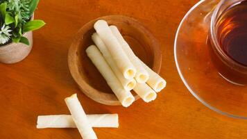 Wafer snack rolls with sweet cheese cream filling serving on plate with a cup of tea for enjoyment isolated on wooden background photo