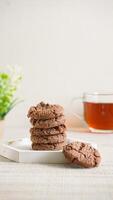 Stack of chocolate cookies on a white plate with a cup of tea isolated on light background photo