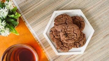 Top view of chocolate cookies on a white plate with a cup of tea for enjoyment isolated on wooden textured background photo