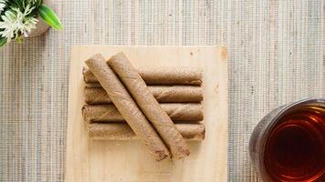 Top view of crispy chocolate wafer roll on a wooden board with a cup of tea isolated on wooden textured background photo