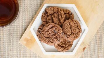 Top view of chocolate cookies on a white plate with a cup tea isolated on wooden textured background photo