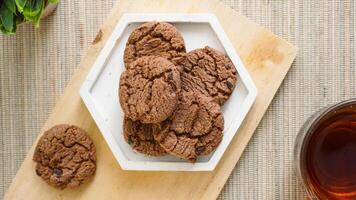 Top view of delicious chocolate cookies on a white plate with a cup tea isolated on wooden textured background photo
