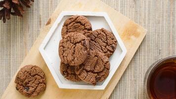 Top view of sweet chocolate cookies on a white plate with a cup tea isolated on wooden textured background photo