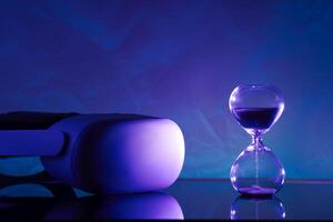 Creative composition featuring a glowing VR headset paired with an hourglass, symbolizing technology and time, on a textured blue backdrop. Perfect for tech, innovation, and timeless concept themes. photo