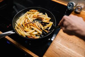 Chef is using spatula to turn batch of golden french fries cooking in non stick pan on modern cooktop, ensuring even browning and crispy texture. Chef turning golden french fries in non stick pan. POV photo