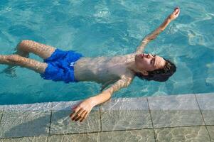 Young Man Relaxing While Floating in a Refreshing Swimming Pool on a Sunny Day photo