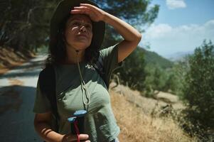 Woman on a Sunny Hiking Trail Shielding Eyes With Hat and Poles photo