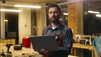 Positive Caucasian wood master man typing laptop online in workshop small business craftsman guy using computer device male joiner worker smile carpenter virtual shopping application Internet website video