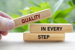 Quality in every step text on wooden blocks held carefully symbolizes continuous improvement and focus photo