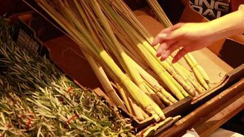 A hand examines and selects lemongrass stalks in a warmly lit supermarket setting video