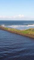 Aerial view of a coastal pathway beside the ocean, capturing waves and greenery under clear skies in Brunswick Heads, Australia video