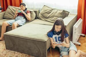 Asian girls relax in cozy room using smartphones with orange curtains, technology education leisure, power outlet with charging cables, game photo